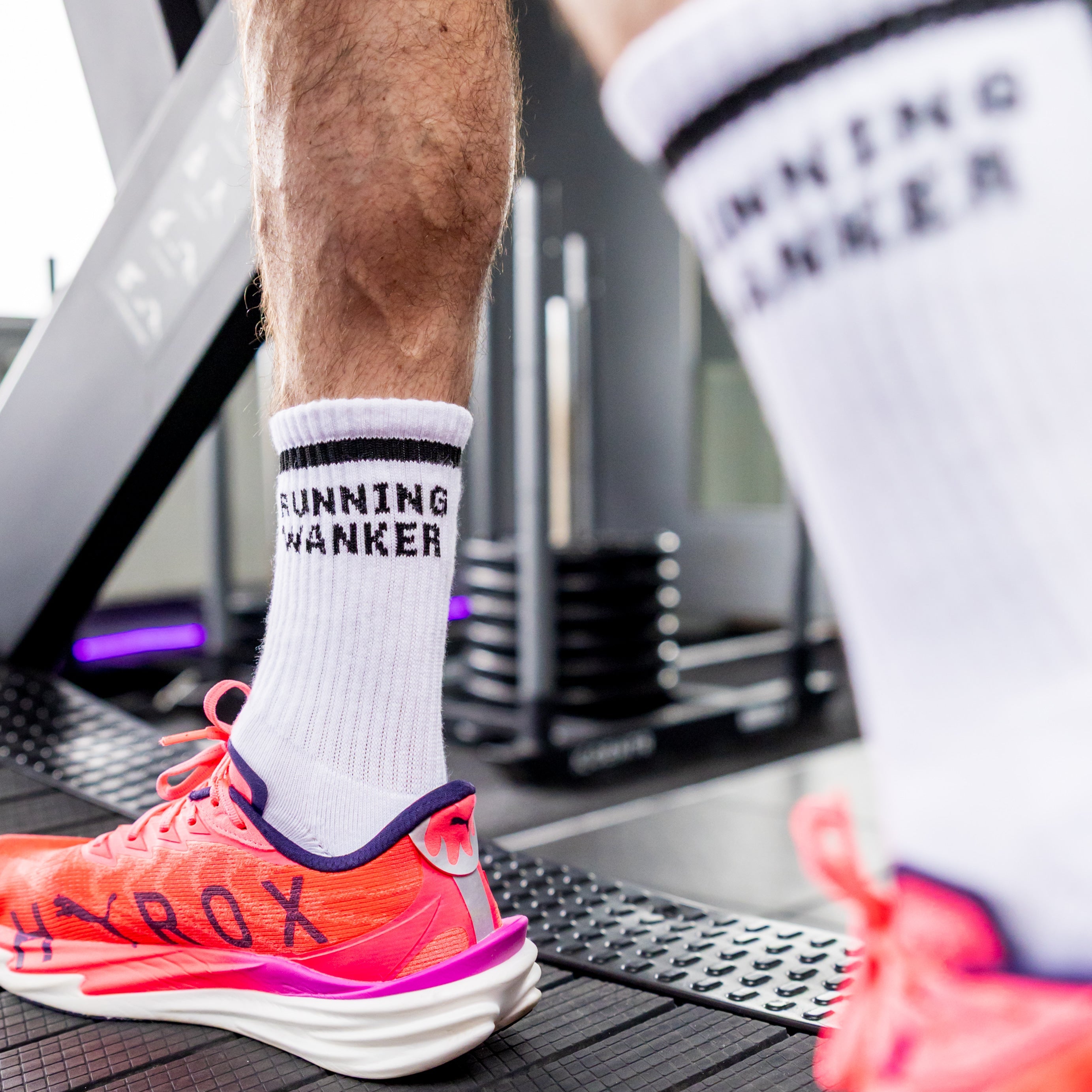 Person wearing white socks with 'RUNNING WANKER' text on a treadmill.